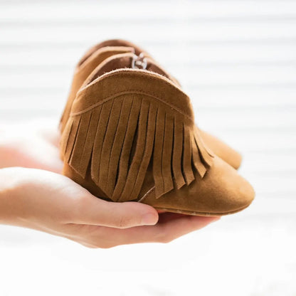A person holding a brown soft sole baby fringe moccasin bootie to highlight the suede fabric texture.