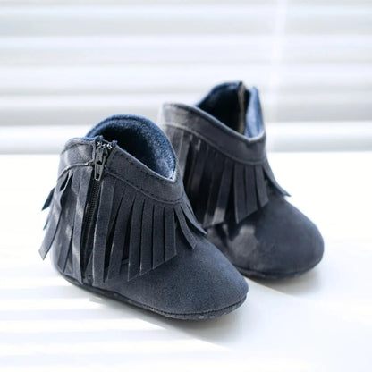 Pair of navy blue infant fringe suede booties sitting next to a window pane.