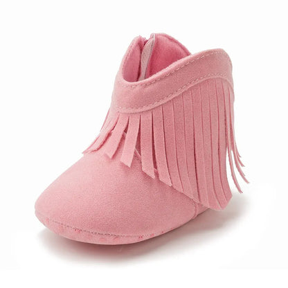 Studio side profile view of a pink infant fringe suede moccasin bootie on a white background.