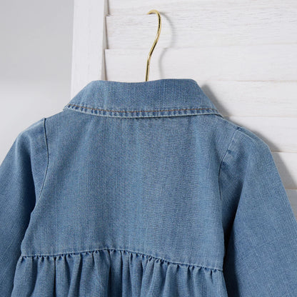 Close-up of the back shoulder and gathered waist detail on a blue denim playsuit hanging on a hanger.