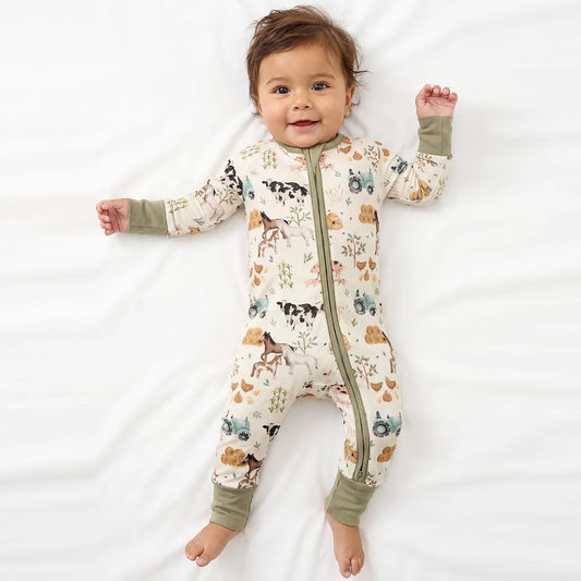 Baby model lying on white sheet wearing Kidsely farm animals and tractors print bamboo viscose zipper romper sleeper