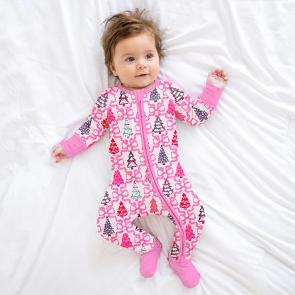 Baby model wearing Kidsely pink Christmas trees and bow print bamboo viscose zipper romper sleeper on white bed sheet