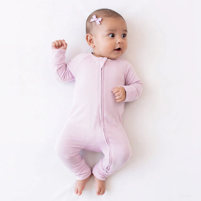 Baby girl model wearing pink bow hair clip and Kidsely solid light pink bamboo viscose zipper romper sleeper on white sheet