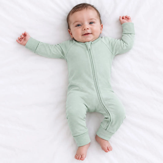 Baby model lying on white sheet wearing Kidsely solid sage green bamboo viscose zipper romper sleeper