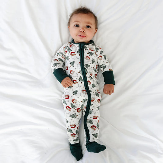 Baby model lying on white sheet wearing Kidsely vintage Santa and Christmas tree print bamboo viscose zipper romper
