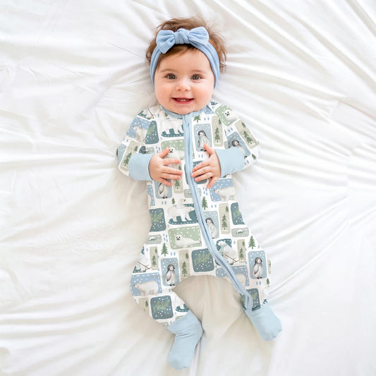 Baby model wearing blue headband and Kidsely winter polar bear and penguin print bamboo viscose zipper sleeper on white sheet