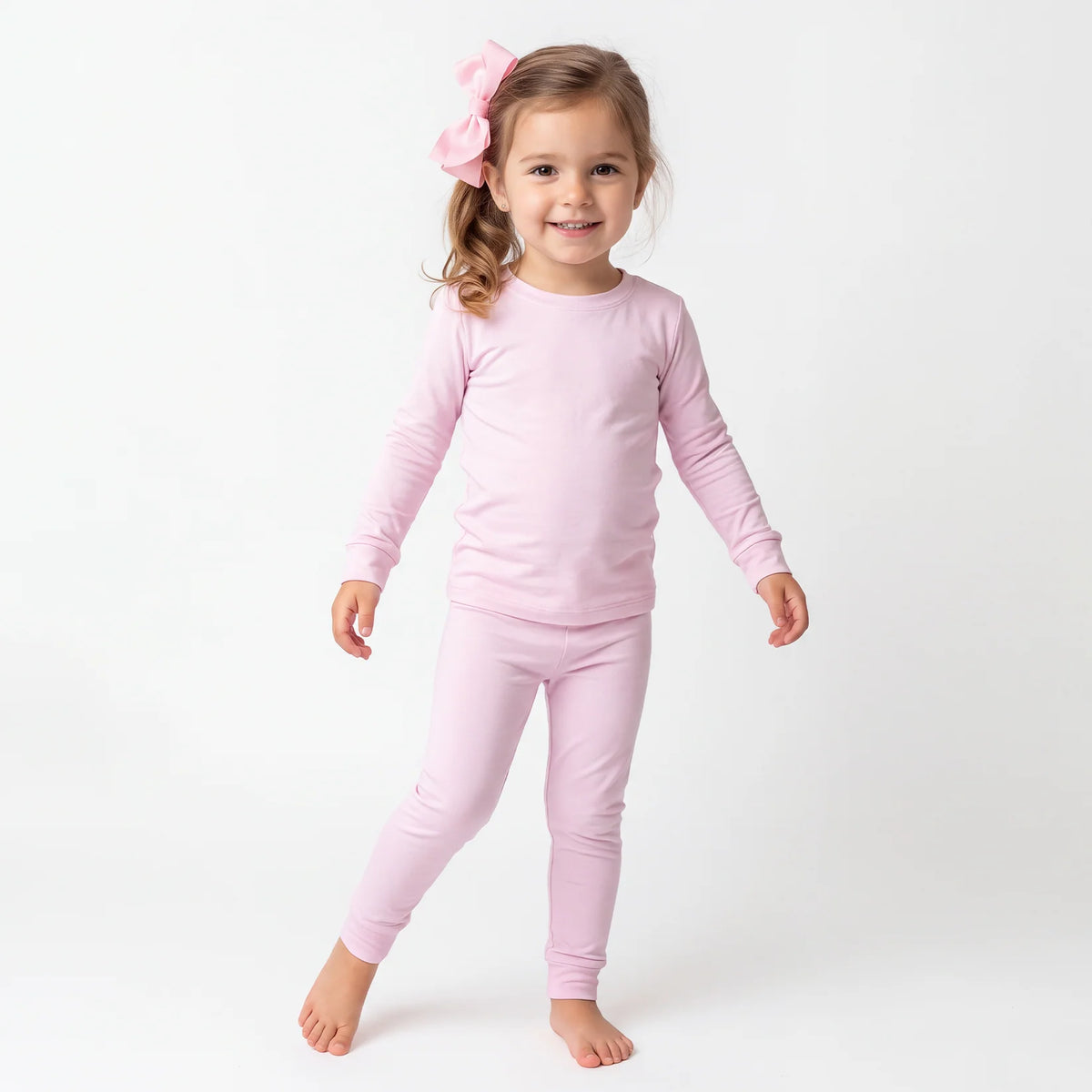Toddler girl model wearing pink hair bow and Kidsely solid light pink bamboo viscose two-piece pajama set