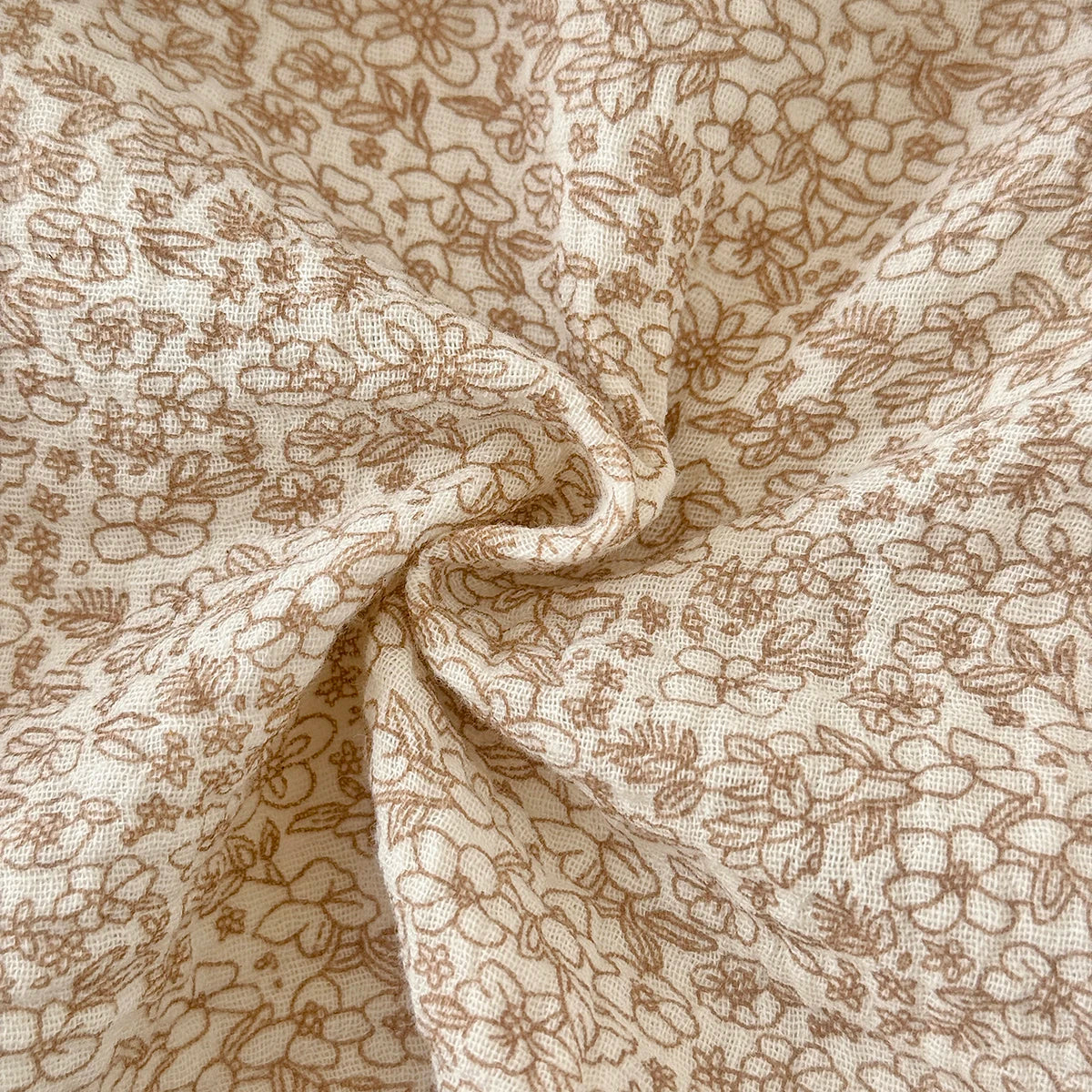 Close-up showing the soft, breathable muslin-like woven texture and earthy beige floral print of the baby romper fabric.