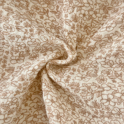 Close-up showing the soft, breathable muslin-like woven texture and earthy beige floral print of the baby romper fabric.