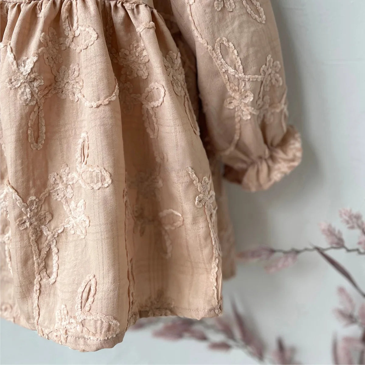 Close-up of the delicate tone-on-tone floral embroidery and ruffled elastic cuff on the beige long sleeve dress.