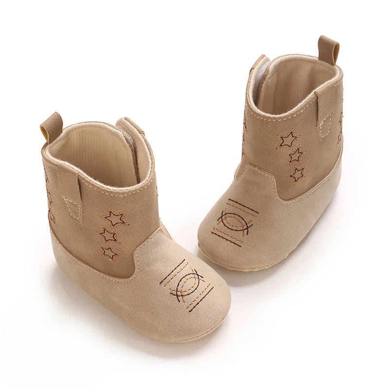 Close up of beige baby cowboy boots on an infant's feet, showing the flexible dotted anti-slip sole.