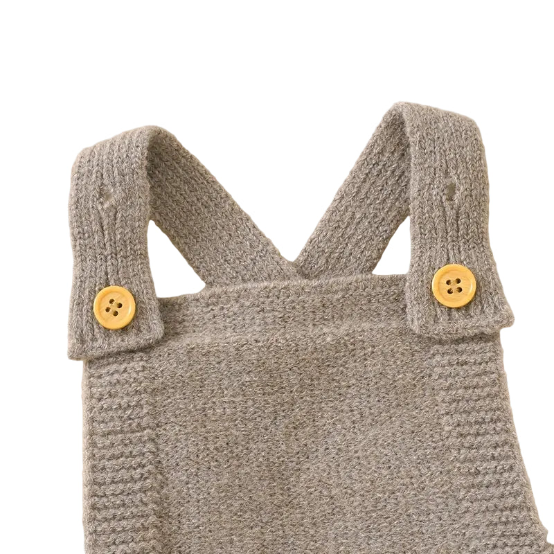 Close-up of the adjustable ribbed shoulder straps and wooden-style buttons on the beige knit baby overalls.