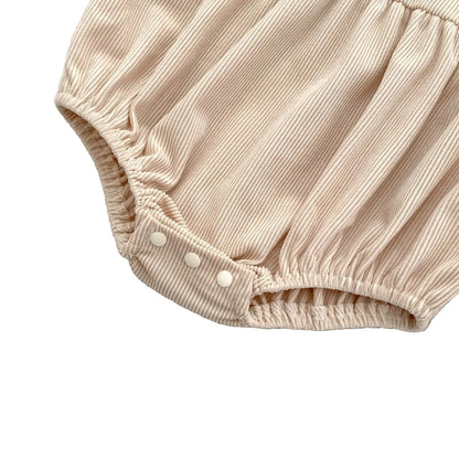 Close-up of the bottom snap closures on the beige ribbed corduroy baby romper designed for easy diaper changes.