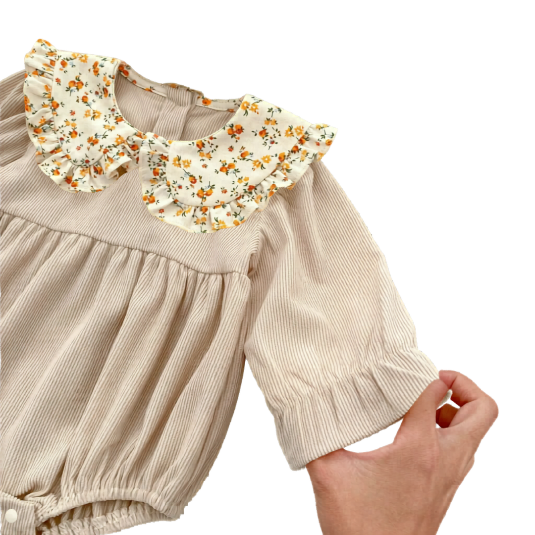 Close-up showing the ruffled sleeve cuff, ribbed texture, and floral Peter Pan collar of the beige baby romper.