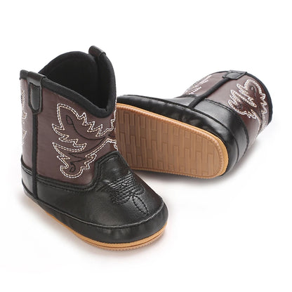 Pair of black and brown toddler cowboy boots with white stitching, showing the textured rubber sole.