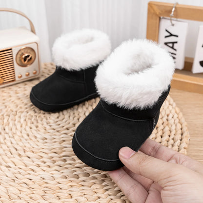 Hand adjusting a pair of black baby soft sole crib boots displayed on a round woven mat.