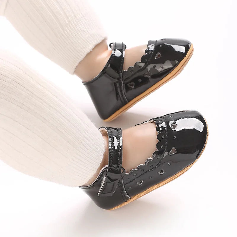 Baby feet wearing glossy black Mary Jane flats with white tights.
