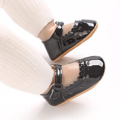 Baby feet wearing glossy black Mary Jane flats with white tights.
