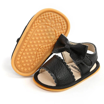 Pair of black leather baby girl first walker sandals with one shoe showcasing the flexible, patterned non-slip rubber outsole.