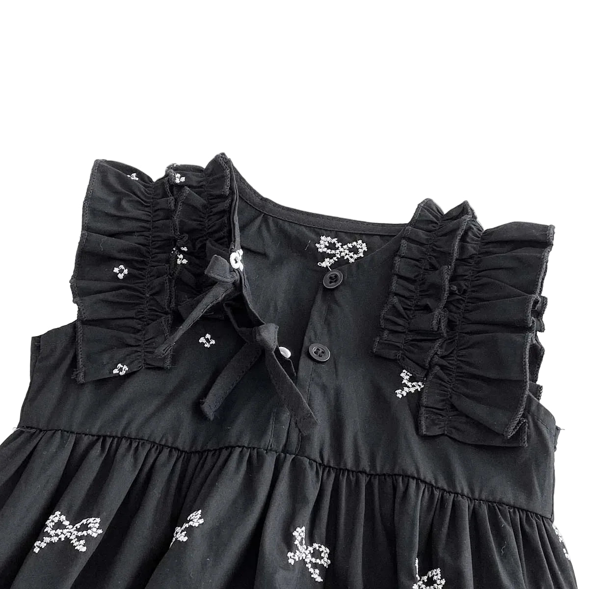Close up of the chest area on a black baby romper showing ruffle sleeves and a cross back tie design.