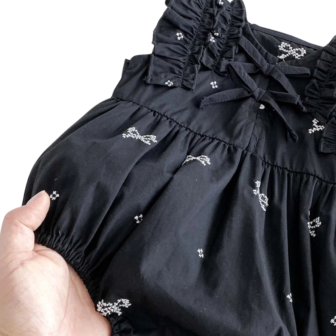 Close up of black woven cotton fabric featuring small white embroidered bow patterns held by a hand.