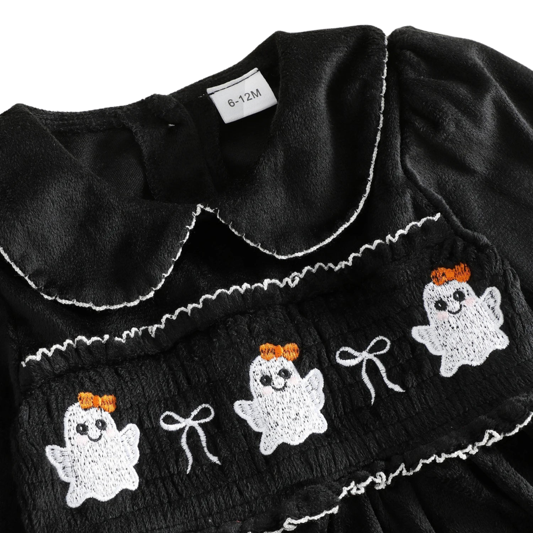 Close-up detail of the intricate white ghost smocked embroidery and delicate bow accents on the chest of the black toddler Halloween dress.