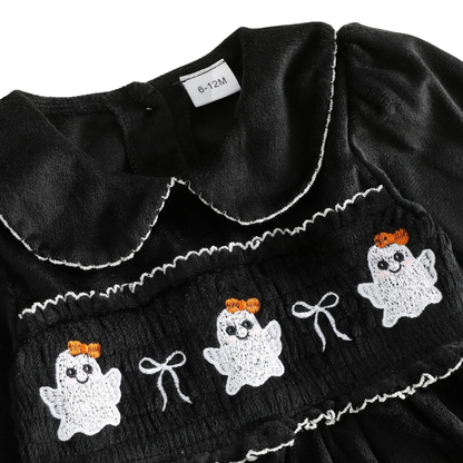 Close-up detail of the intricate white ghost smocked embroidery and delicate bow accents on the chest of the black toddler Halloween dress.