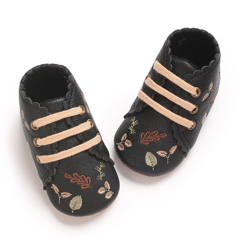Top-down view of black scalloped baby girl crib shoes.