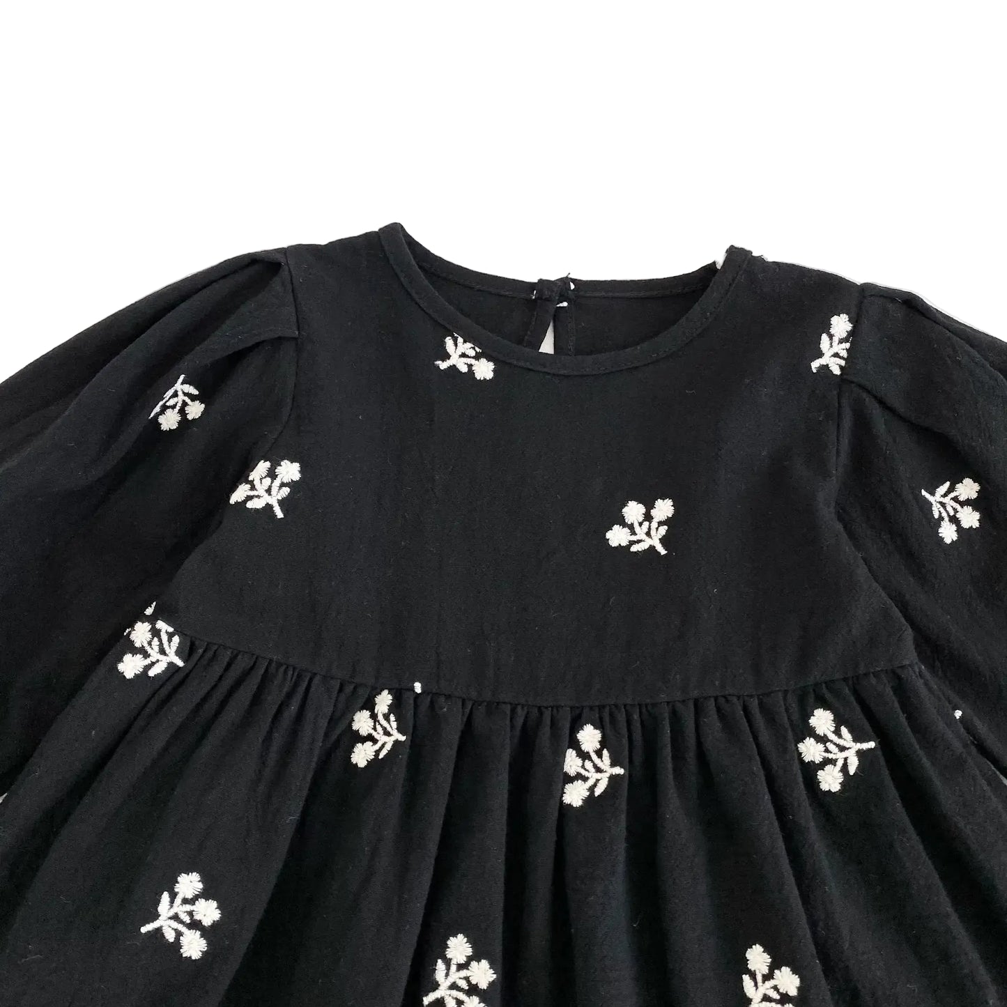 Close-up of the round neckline and white floral embroidery on the front bodice of the black toddler dress.