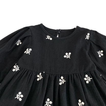 Close-up of the round neckline and white floral embroidery on the front bodice of the black toddler dress.