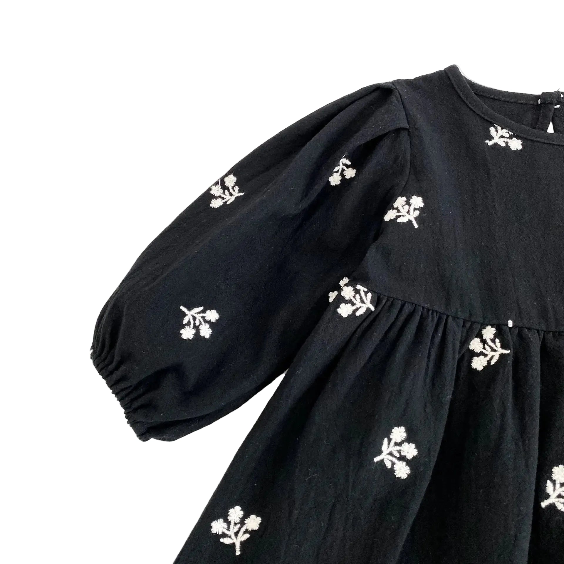Detail shot of the long puff sleeve with white floral embroidery on the black toddler dress.