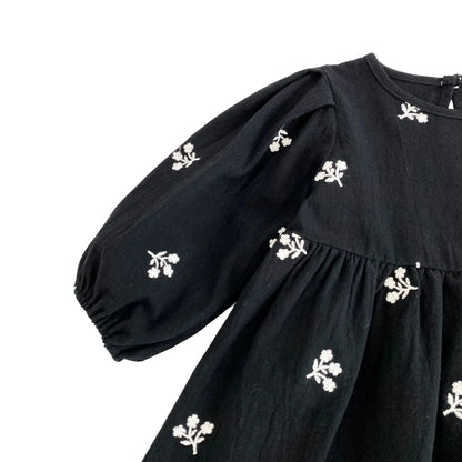 Detail shot of the long puff sleeve with white floral embroidery on the black toddler dress.
