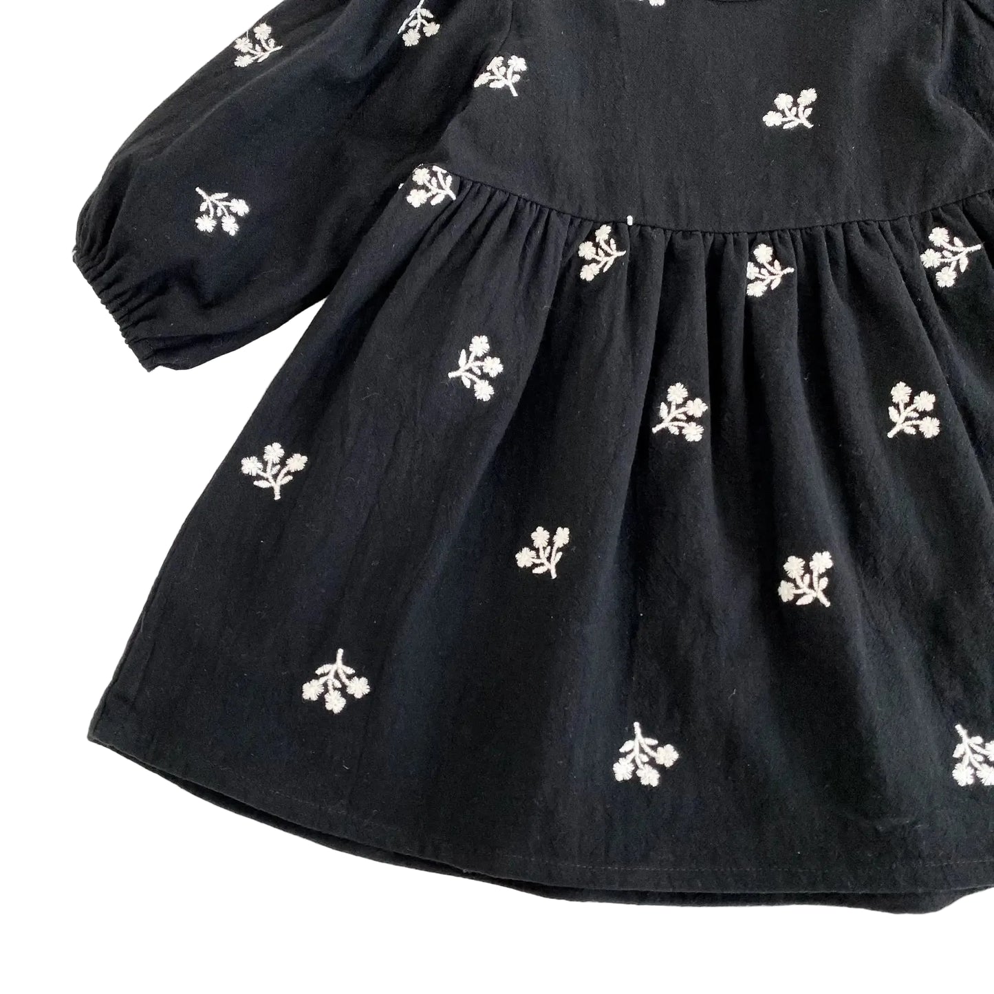 Close-up of the flowing skirt fabric and white floral embroidery on the black babydoll dress.