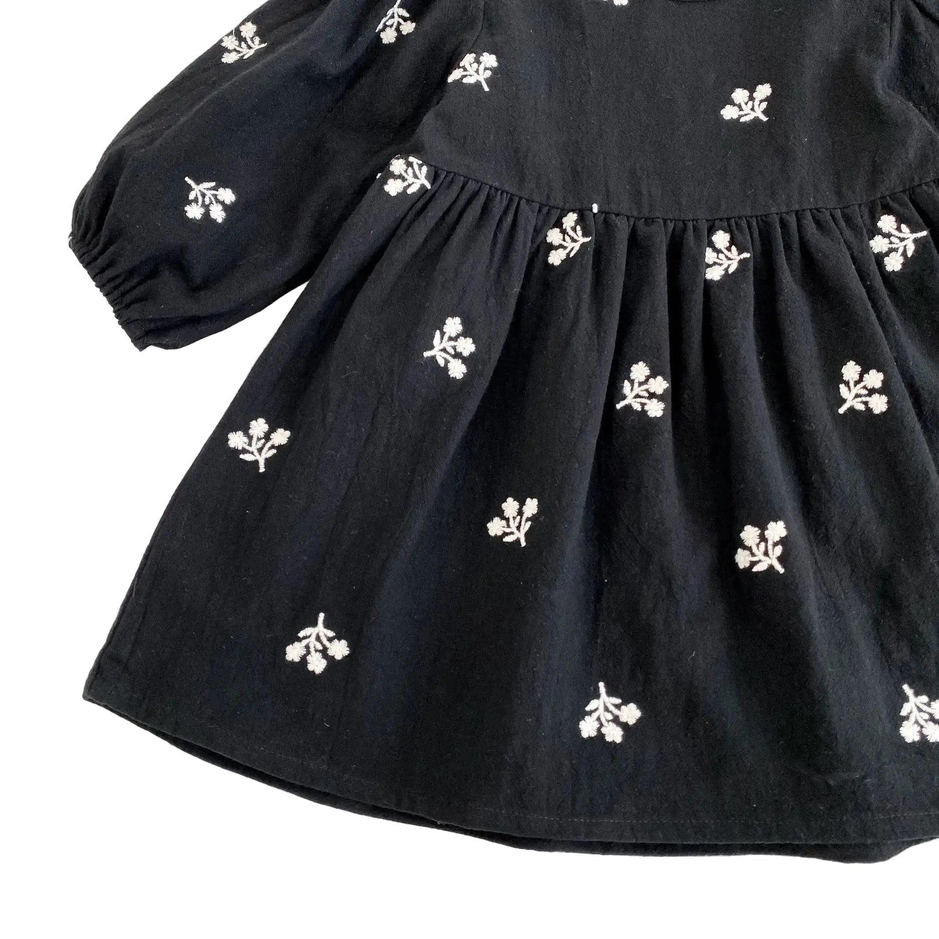Close-up of the flowing skirt fabric and white floral embroidery on the black babydoll dress.
