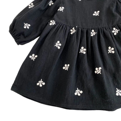 Close-up of the flowing skirt fabric and white floral embroidery on the black babydoll dress.