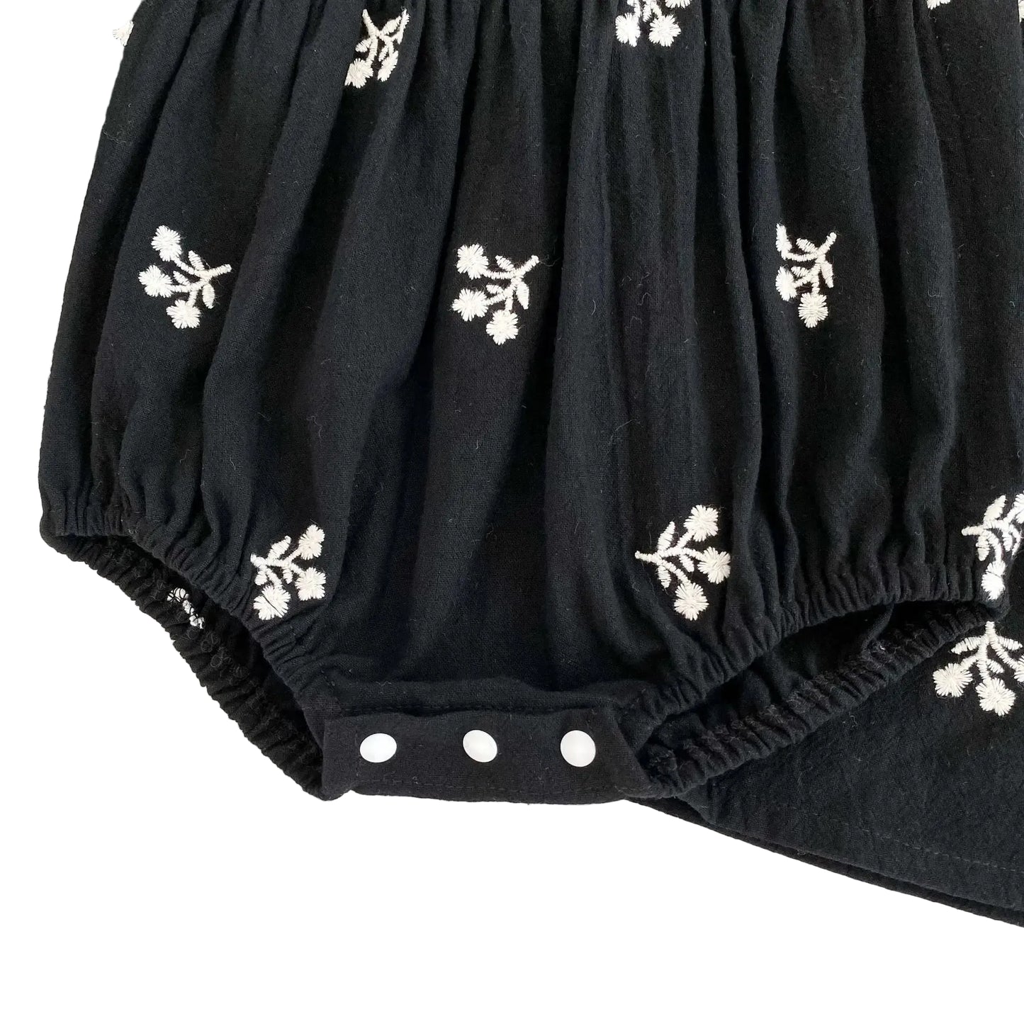Close-up of the closed three-snap bottom closure on the baby girls black floral bubble romper.
