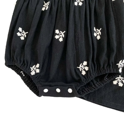 Close-up of the closed three-snap bottom closure on the baby girls black floral bubble romper.