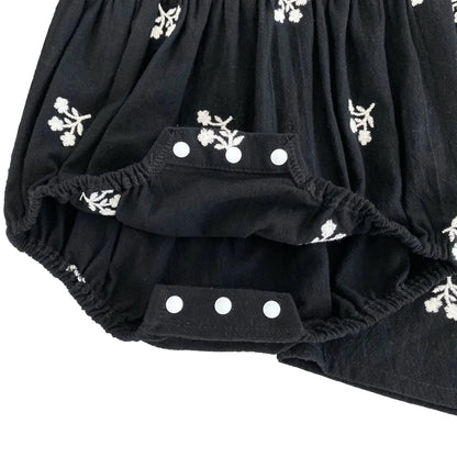 Close-up of the open three-snap bottom closure showing the interior crotch opening of the baby girls black romper.