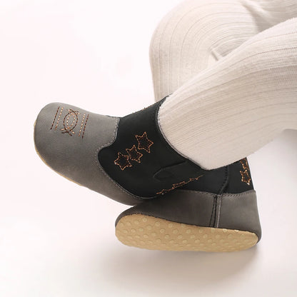 Close up of a baby wearing black and grey soft sole western booties, showing the gentle anti-slip bottom for pre-walkers.