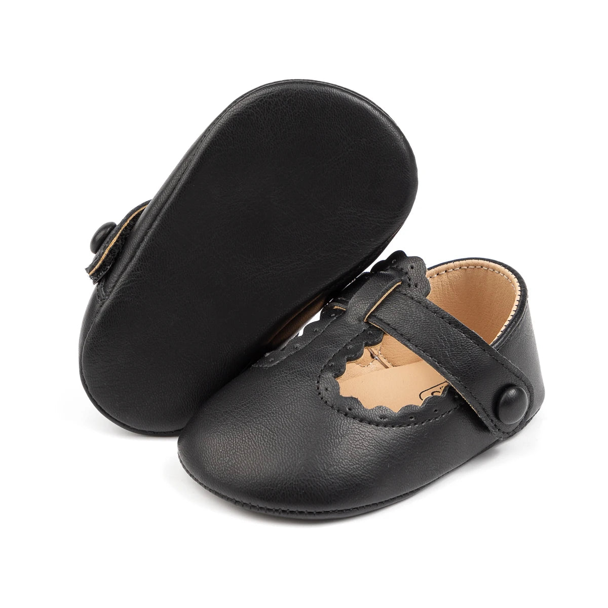 air of black baby girl first walker shoes, with one shoe resting on its side to display the flexible black soft sole bottom.