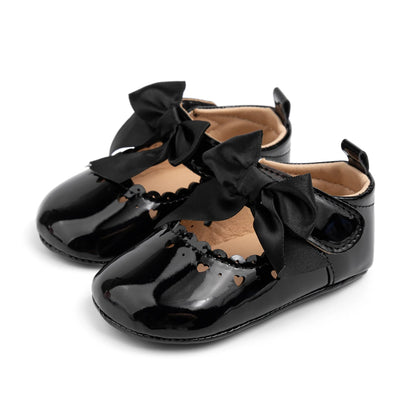 Pair of glossy black PU leather infant Mary Jane dress shoes featuring a satin bow and heart cutouts.