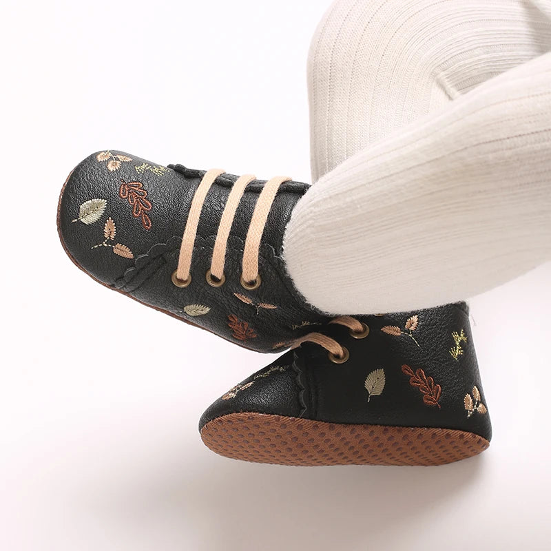 Baby wearing black embroidered soft sole pre-walker booties.