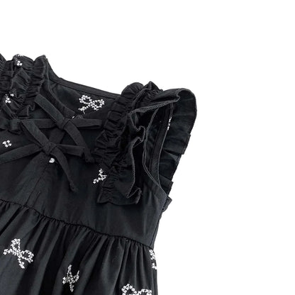 Close up of the ruffle shoulder sleeves and embroidered white bows on a black cotton baby bodysuit.
