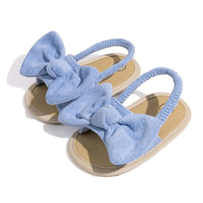 Pair of light blue baby girl soft sole sandals with an oversized brushed fabric bow and elastic strap.