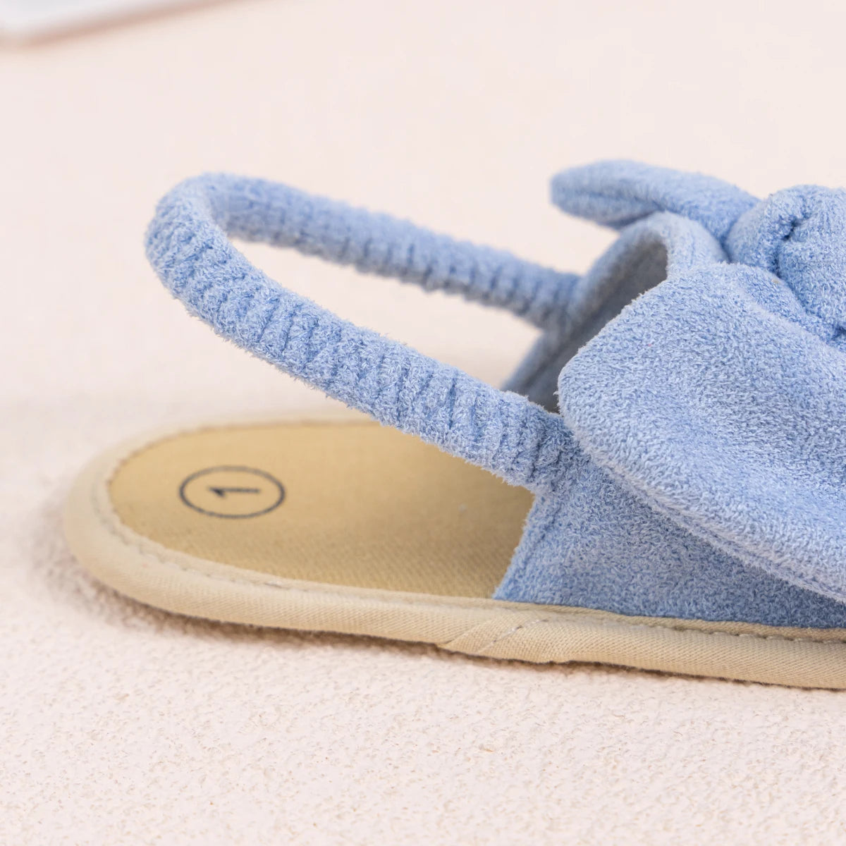 Close-up of the stretchy brushed fabric elastic slingback heel strap on a light blue infant sandal.