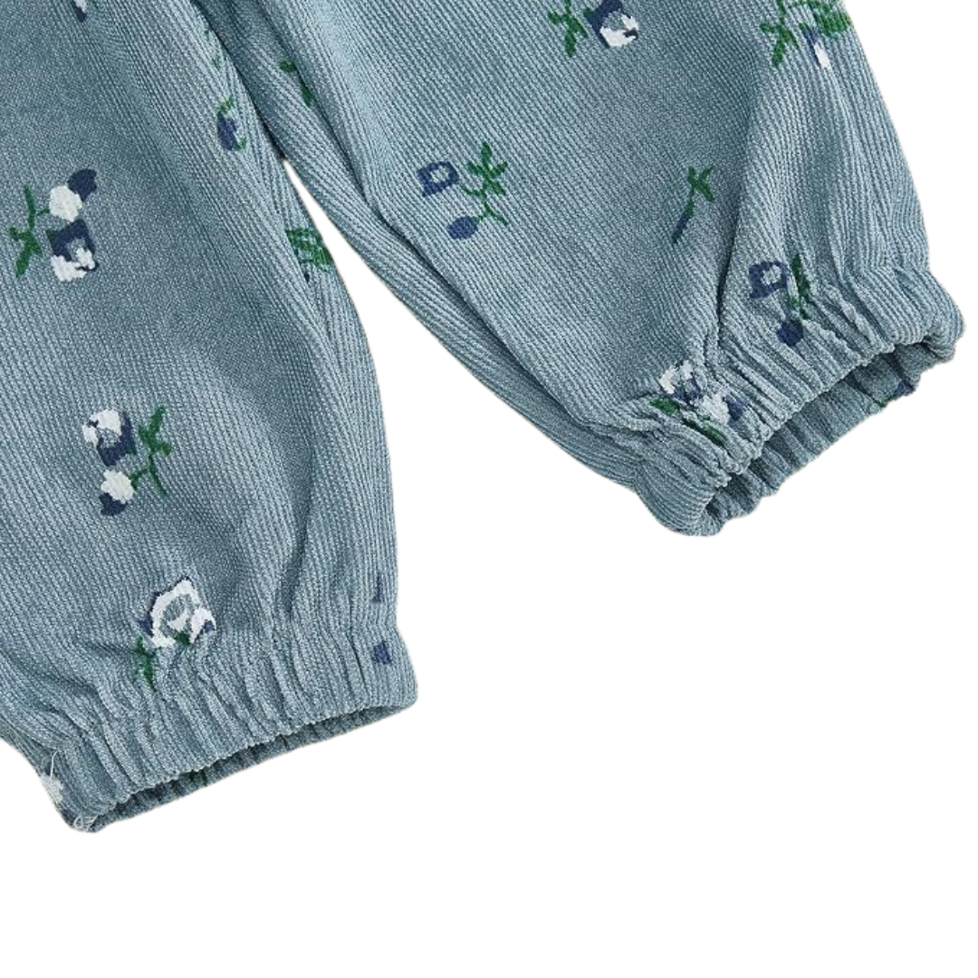 Close-up of dusty blue floral corduroy fabric on baby girl pants showing the ribbed texture, floral print, and elastic ankle cuffs.
