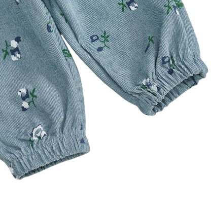 Close-up of dusty blue floral corduroy fabric on baby girl pants showing the ribbed texture, floral print, and elastic ankle cuffs.