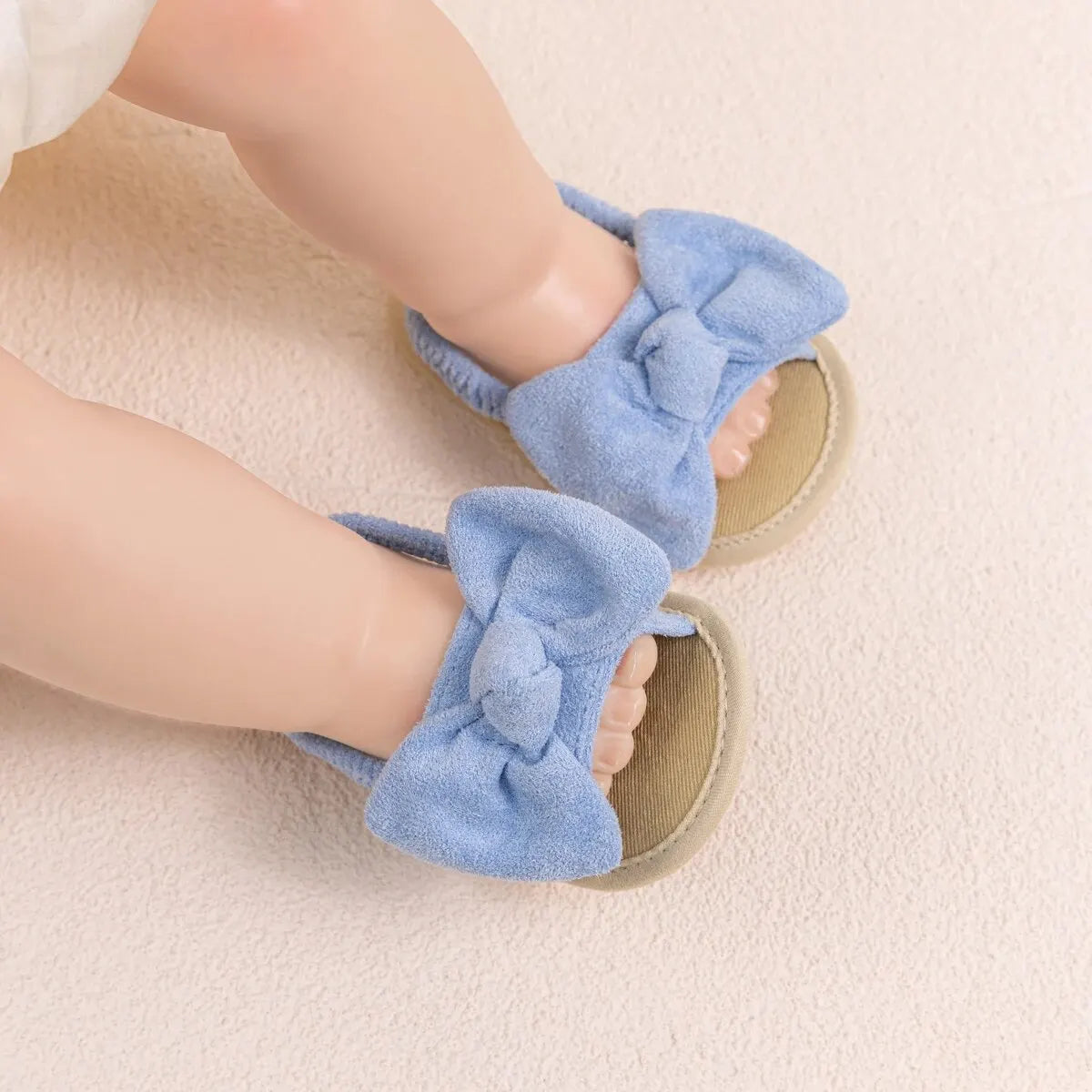 Infant wearing light blue soft sole sandals with a bow, showing a secure and comfortable fit.