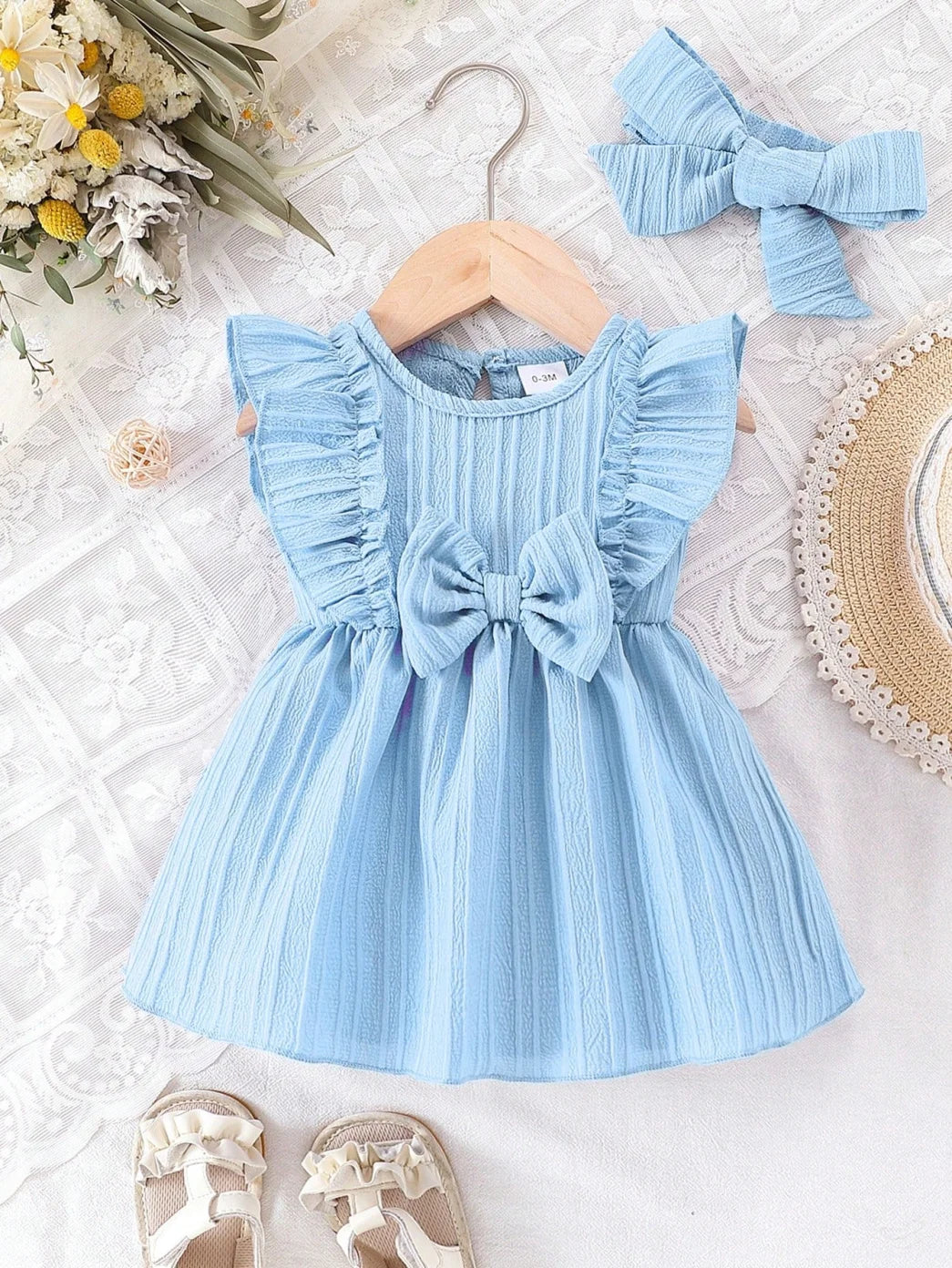 Front view of the light blue infant and toddler sleeveless ruffle dress with center bow, displayed on a wooden hanger.