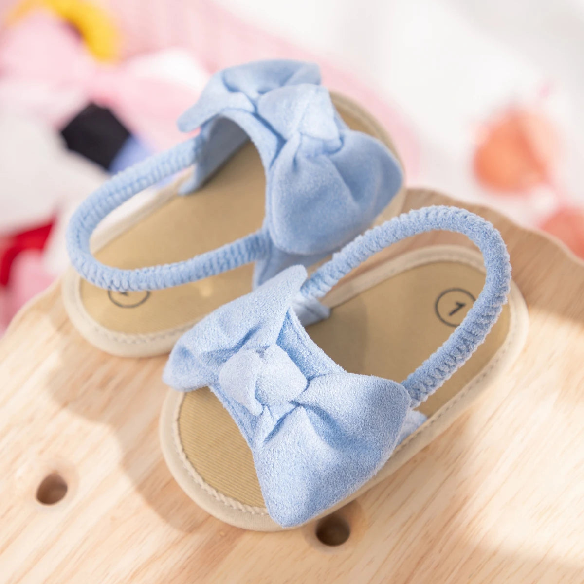 Light blue baby girl soft sole bow sandals resting on a natural wood surface.
